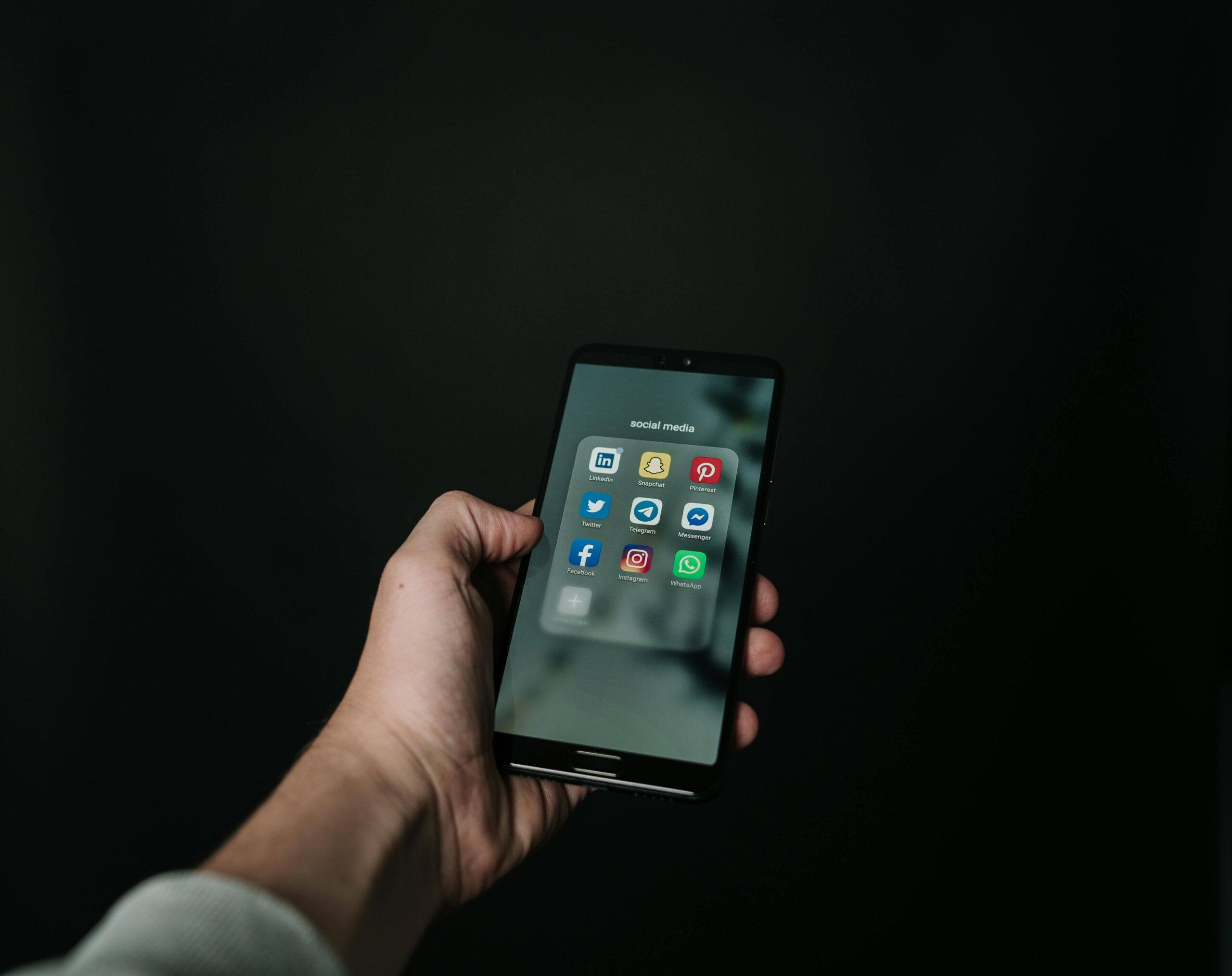 pexels photo 2818118 2818118 Close-up of a hand holding a smartphone displaying various social media app icons on a dark background.